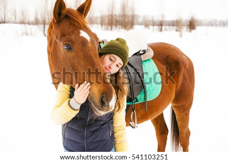Female rider and horse in the open air. portrait of a beautiful young woman with her stallion, outdoors in winter.
