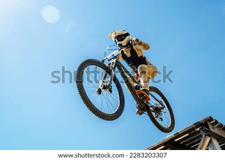 female rider on downhill bike jumping wooden drop, background blue sky, racing DH mountain bike, extreme sport games