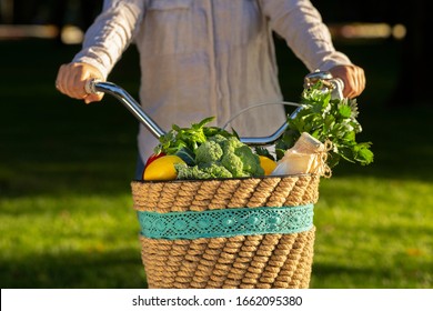 Female Riding A Bike With Fresh Vegetables From Market, Green Grass Background