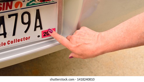 A female right index finger pressing the required annual license registration on rear license plate.