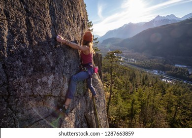 Female Rock climber climbing on the edge of the cliff during a sunny winter sunset. Taken in Area 44 near Squamish and Whistler, North of Vancouver, BC, Canada.