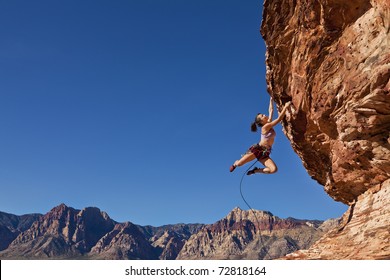 Female rock climber dangling on the edge of a steep cliff struggles for her next grip.