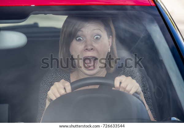 female rookie new driver young beautiful woman\
scared and stressed while driving car in fear and shock face\
expression screaming in\
panic