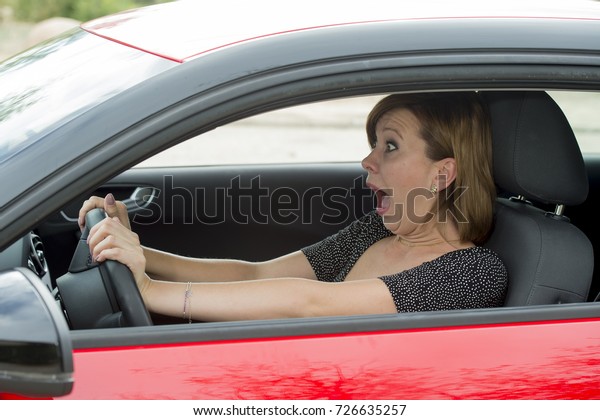 female rookie new driver young beautiful woman\
scared and stressed while driving car in fear and shock face\
expression screaming in\
panic