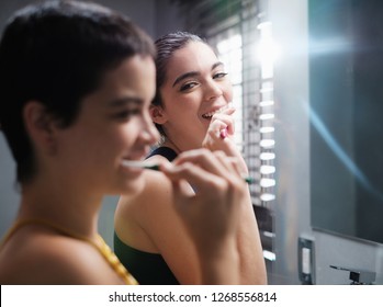 Female Roomates In Bathroom Brushing Teeth Together. A Pair Of Young Lesbian Women Couple Cleaning Teeth With A Toothbrush In Restroom At Morning. Concept Of Dental Hygiene And Same Sex Relationships