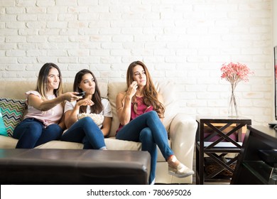 Female Roomates Relaxing At Home While Watching Tv And Eating Popcorn