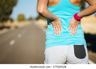 Female runner athlete back injury and pain. Woman suffering from painful lumbago or kidney illness while running in rural road. - Powered by Shutterstock