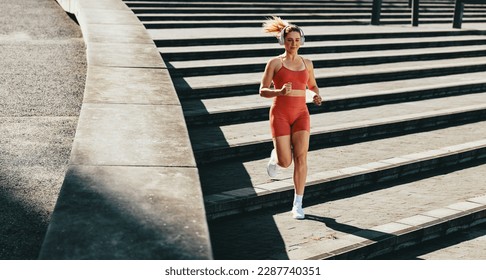 Female runner burning calories with a cardio workout. Sporty woman jogging down the stairs outdoors. Woman exercising with headphones on in the morning. - Powered by Shutterstock