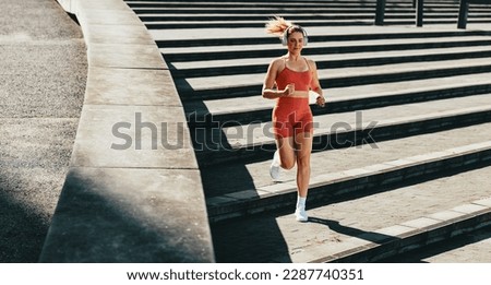 Female runner burning calories with a cardio workout. Sporty woman jogging down the stairs outdoors. Woman exercising with headphones on in the morning.