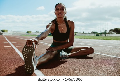 Female runner doing stretching exercises sitting on running track. Woman runner sitting on running track and stretching her leg. - Powered by Shutterstock