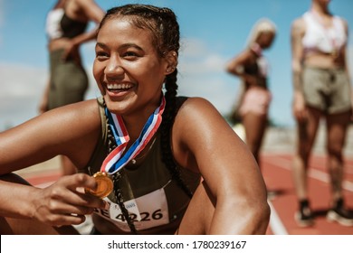 Female runner with a gold medal sitting on track. Running race winner sitting on track with athletes in background.