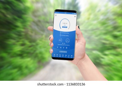 Female runner holding smartphone and checking progress while running in park