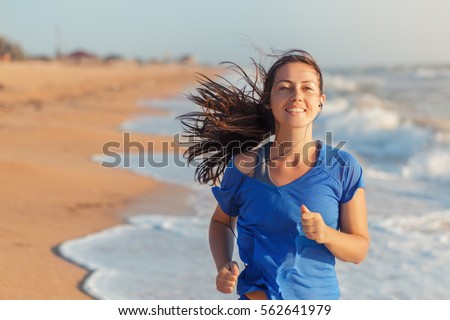 Female runner jogging during outdoor workout on beach listening to music in earphones. Healthy active lifestyle girl