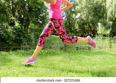 Female runner running shoes and legs in city park. Woman jogging wearing floral capris leggings compression tights and pink running shoes.