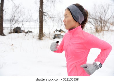 Female Runner Trail Running In Cold Snowing Weather. Asian Chinese Athlete Woman Training For Marathon Jogging Outside In Snow Wearing Activewear Jacket, Headband, And Winter Gloves.