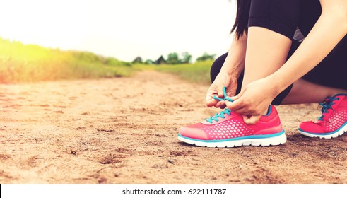 Female runner tying her running shoes on a sandy trail - Powered by Shutterstock