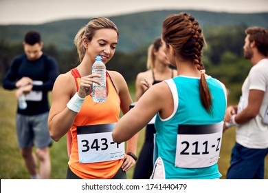 Female Runners Communicating Before Marathon Race In Nature. Focus Is On Woman With Water Bottle. 