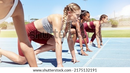Female runners at the starting line of an olympic race. Athletes kneeling ready to start running. Focused women prepared to compete in a track and field event. Sportswomen on the starting block