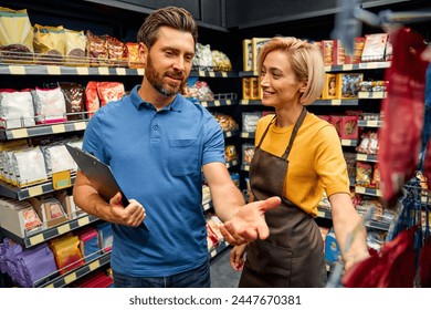 A female sales worker in uniform stands with a sales representative and discusses the delivery of goods. Shopping for food in a supermarket. - Powered by Shutterstock