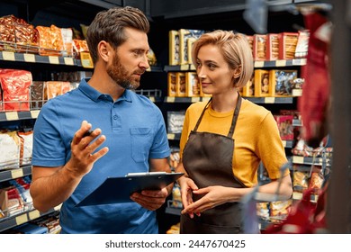 A female sales worker in uniform stands with a sales representative and discusses the delivery of goods. Shopping for food in a supermarket. - Powered by Shutterstock