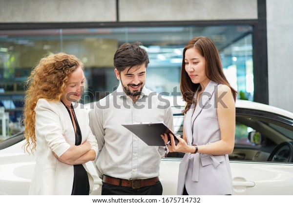 The female salesperson is\
offering a Price list for the customer to buy a new car. signing a\
document and talking to sales manager while buying a new car in\
dealership