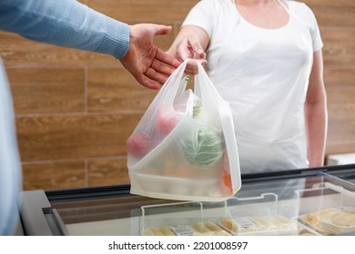 Vendedora de sexo femenino con bolsas de plástico y verduras frescas de mano en mano. El hombre está comprando en una tienda de comestibles. Cierre del moderno paquete biodegradable utilizado en la tienda.