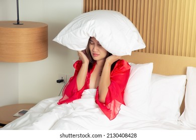 Female In A Satin Red Nightgown Lying On Bed And Closing Her Head With The Pillow At Night. Asian Woman Suffering From Insomnia Or Depression.