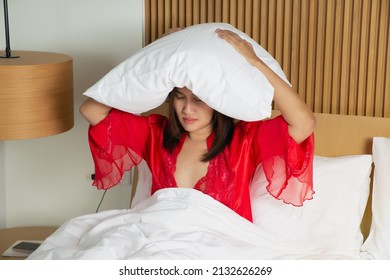 Female In A Satin Red Nightgown Lying On Bed And Closing Her Head With The Pillow At Night. Asian Woman Suffering From Insomnia Or Depression.