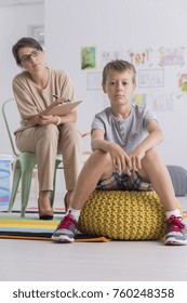 Female School Psychologist And Rebellious Little Boy Sitting In Class, Serious Young Child Looking At Camera