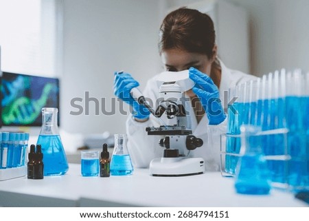 Female scientist analyzing sample using a microscope and pipette, surrounded by test tubes and beakers in a modern lab setting