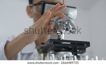 Female scientist analyzing test samples under microscope in contemporary research environment of laboratory. Medicine, healthcare and science concept