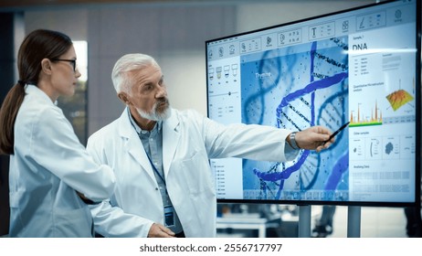 Female Scientist Discussing Ideas in a Biotech Startup Lab. Student Listening to Her Senior Science Professor while He Shows DNA Sequencing Method on a TV Screen