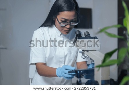 A female scientist examines samples using a microscope in a biotechnology laboratory focused on pharmaceutical medical research and biotechnology.