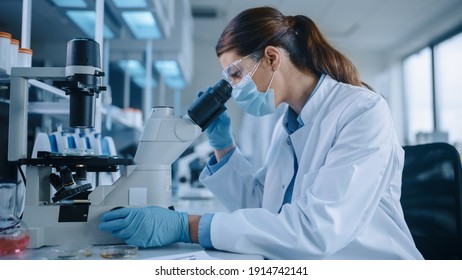 Científica en máscara facial y gafas mirando un plato de petri con muestras de químicos modificados genéticamente bajo un microscopio. Microbiólogo trabajando en laboratorio moderno con equipo tecnológico.