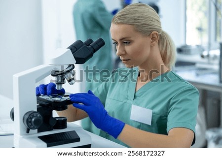 Female scientist in lab using microscope for microscopic view of biochemical samples