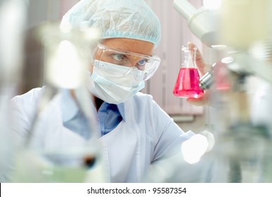 Female Scientist Looking Closely At A Beaker With Pink Fluid