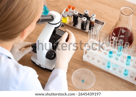 Female scientist looking through microscope at table in laboratory, closeup