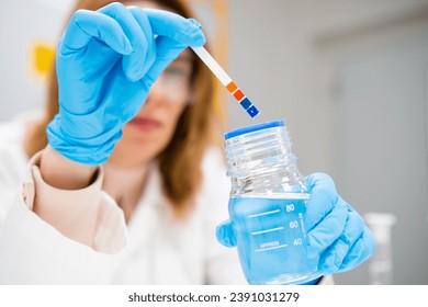 Female scientist measures pH of the solution using indicator paper