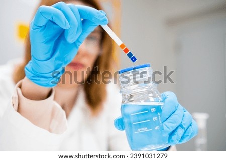 Female scientist measures pH of the solution using indicator paper