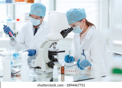 Female Scientist With A Petri Dish Sitting At A Laboratory Table .