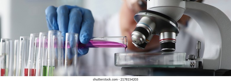 Female scientist pouring pink sample liquid on glass container under microscope in lab - Powered by Shutterstock