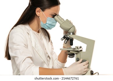 Female Scientist With Protective Face Mask Looking Through A Microscope, White Background