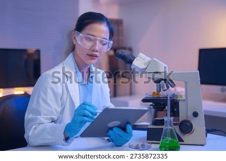 Female scientist using a microscope to analyze samples and writing on document.
