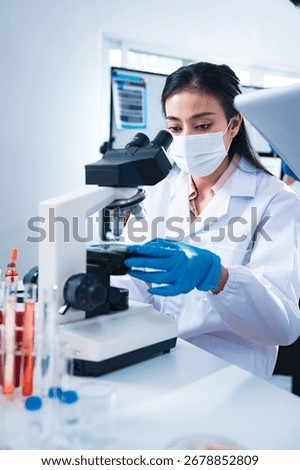 Female scientist using a microscope to examine a blood sample while a colleague records data, symbolizing teamwork, healthcare diagnostics, virus testing, and innovation in medical research.