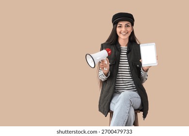 Female scriptwriter with blank tablet computer and megaphone sitting on beige background