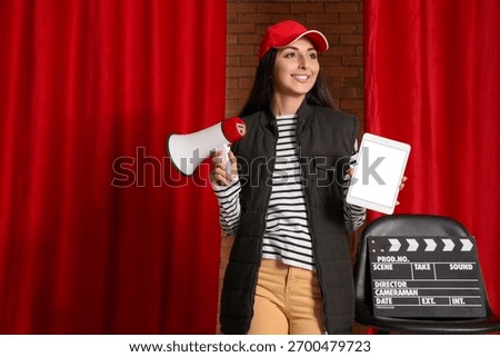Female scriptwriter with blank tablet computer and megaphone near red curtains
