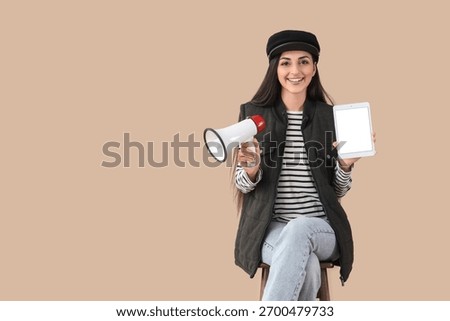Female scriptwriter with blank tablet computer and megaphone sitting on beige background