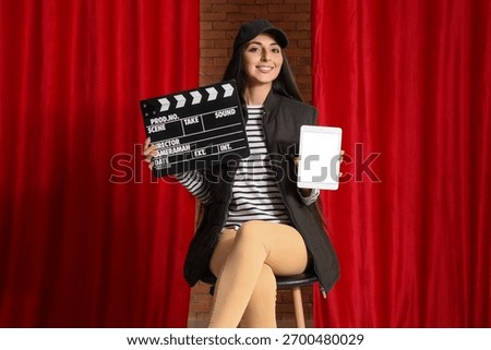 Female scriptwriter with blank tablet computer and movie clapper near red curtains