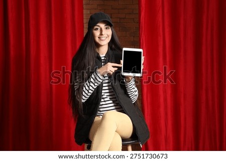 Female scriptwriter pointing at blank tablet computer near red curtains