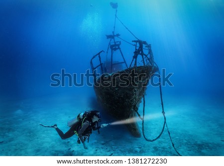 A female scuba diver explores a sunken shipwreck in the deep, blue sea